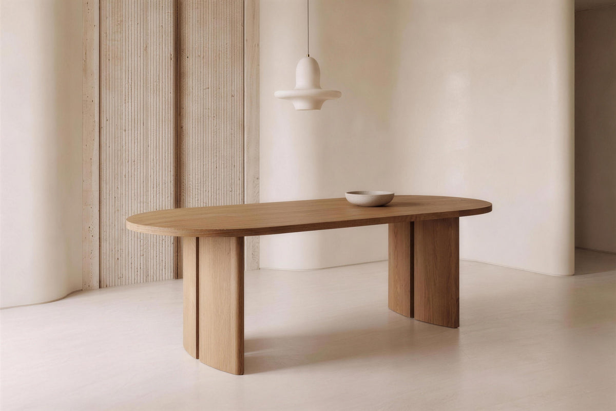The Radda Oval Dining Table in light oak in a plaster and travertine dining room