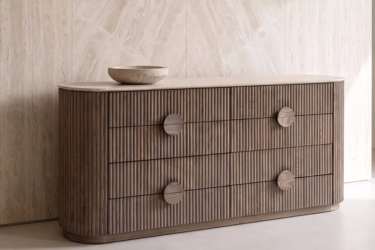 The Spello Fluted Travertine Wide Chest of Drawers against a travertine wall
