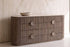 The Spello Fluted Travertine Wide Chest of Drawers against a travertine wall