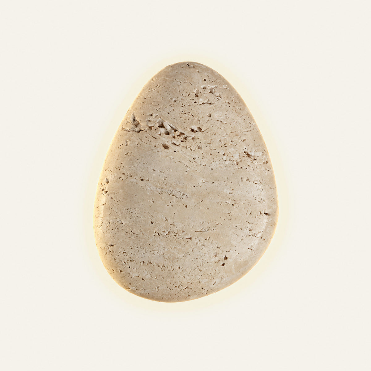 The Uovo travertine wall light, an egg-shaped stone pebble with a halo of light